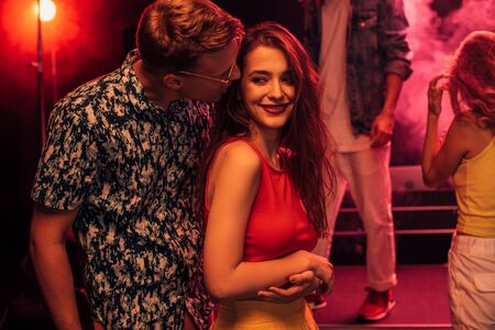 man kissing on cheek young woman during rave party in nightclubの写真素材