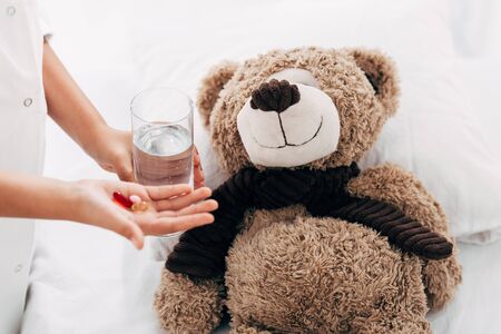 partial view of child giving glass of water and pills to teddy bearの写真素材