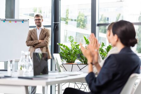 smiling businessman in glasses standing with crossed arms near flipchart during conferenceの写真素材