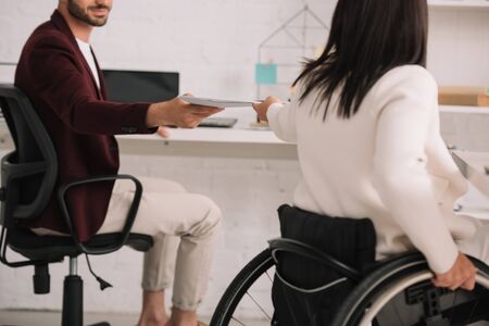 cropped view of disabled businesswoman giving documents to colleague in officeの写真素材