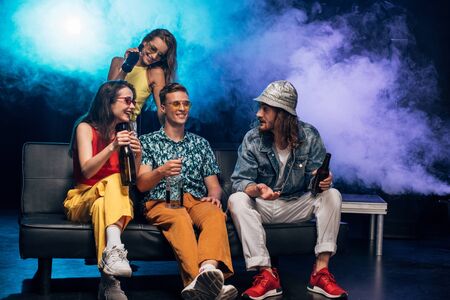 happy young women and men with alcohol sitting on couch in nightclub