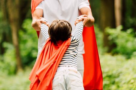 cropped view of father spinning around small boy in red cloakの写真素材