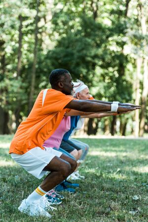 selective focus of african american man doing sit ups with pensioners in parkの写真素材