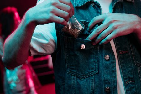 Cropped view of man putting in pocket marijuana in nightclub