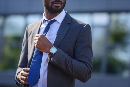 cropped view of african american businessman touching tie while standing on streetの写真素材