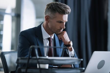 selective focus of handsome man in formal wear using laptop in office
