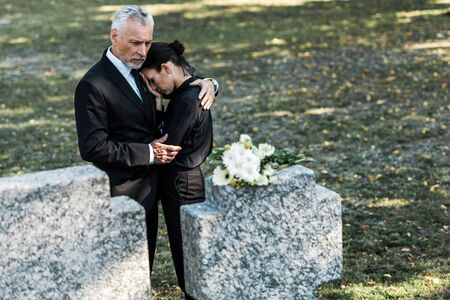 selective focus of bearded man in suit hugging attractive woman and tombsの写真素材