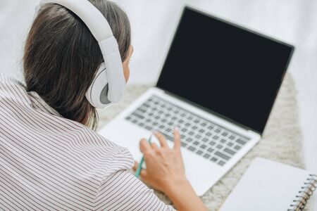 back view of woman with headphones using laptop and holding pencilの写真素材