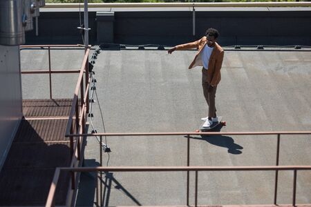 stylish african american businessman riding longboard on sunny rooftopの写真素材