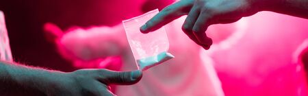panoramic shot of man passing drugs in plastic zipper bag to man in nightclub
