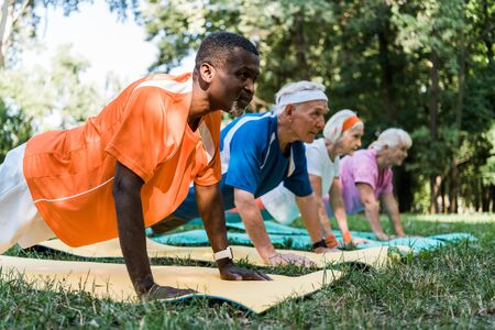 selective focus of african american man doing plank exercise with retired pensioners on fitness matsの写真素材