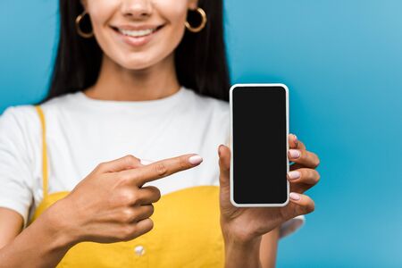 cropped view of girl pointing with finger at smartphone with blank screen isolated on blue