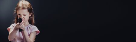 panoramic shot of kid holding pistol while looking at camera on black backgroundの写真素材