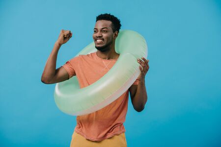 happy african american man with swim ring gesturing while celebrating isolated on blueの写真素材