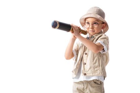 curious smiling explorer boy in glasses and hat holding spyglass isolated on whiteの写真素材
