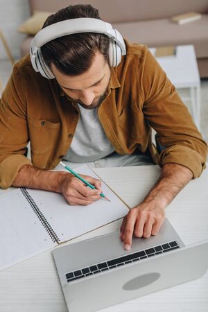 high angle view of man listening music, writing in notebook and using laptopの写真素材