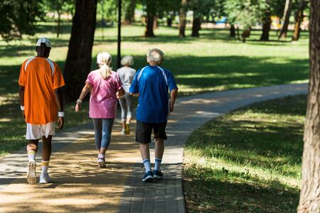 back view of retired multicultural pensioners in sportswear walking in walkway in parkの写真素材