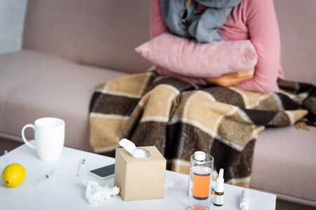cropped view of ill woman with grey scarf sitting on sofa and holding pillowの写真素材