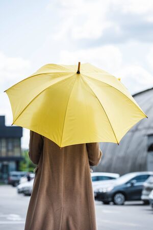 back view of woman in coat holding yellow umbrellaの写真素材
