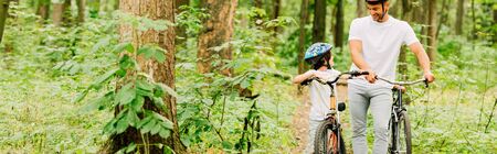 panoramic shot of father and son walking with bicycles in forestの写真素材