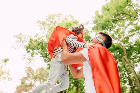 father in superhero costume catching son with handsの写真素材