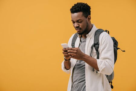 handsome african american man with backpack using smartphone isolated on orangeの写真素材