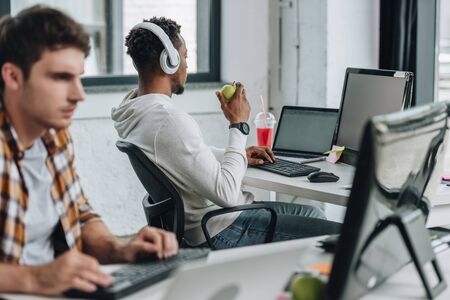 selective focus of young african american programmer in headphones working near colleague in officeの写真素材