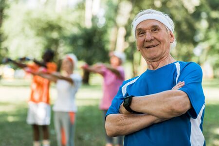 selective focus of happy senior man standing with crossed arms in parkの写真素材