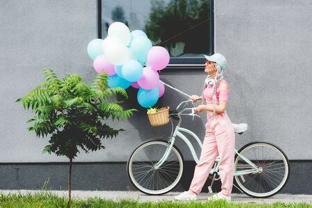stylish girl with bicycle and balloons near buildingの写真素材