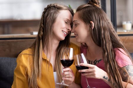 two lesbians holding wine glasses while sitting on sofa in living roomの写真素材