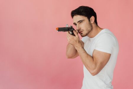 muscular man in white t-shirt aiming gun isolated on pink