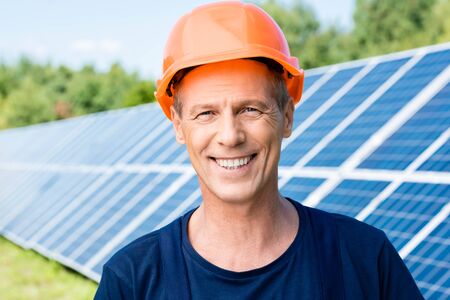 handsome engineer in t-shirt and orange hardhat smiling and looking at camera