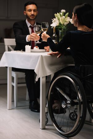 back view of disabled young woman clinking glasses of white wine with boyfriend during romantic dinnerの写真素材