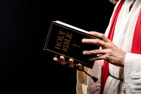 cropped view of man holding book with holy bible letters isolated on blackの写真素材