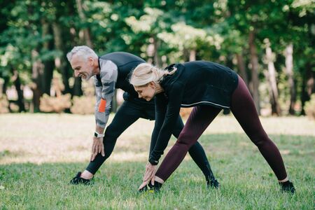 positive, mature sportsman and sportswoman stretching in park togetherの写真素材
