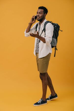 curly african american man talking on smartphone while standing on orangeの写真素材