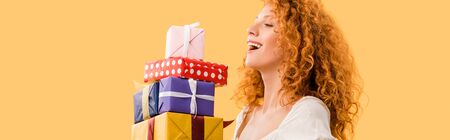 laughing redhead girl holding presents isolated on yellowの写真素材