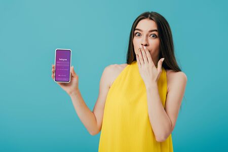 KYIV, UKRAINE - JUNE 6, 2019: shocked beautiful girl in yellow dress showing smartphone with Instagram app isolated on turquoiseのeditorial素材