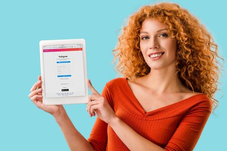 KYIV, UKRAINE - JULY 16, 2019: smiling redhead woman holding digital tablet with instagram app,...