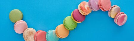 top view of multicolored delicious French macaroons in curved line on blue bright background with copy space, panoramic shotの写真素材