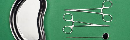 panoramic shot of scissors and dental mirror near metallic plate isolated on green