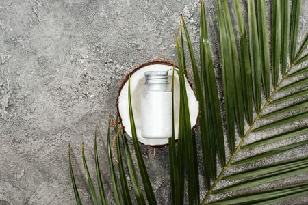 top view of cream in bottle on coconut half on grey textured background with green palm leafの写真素材
