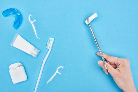 cropped view of woman holding tweezers with cotton pad near toothpaste and toothbrush on blue