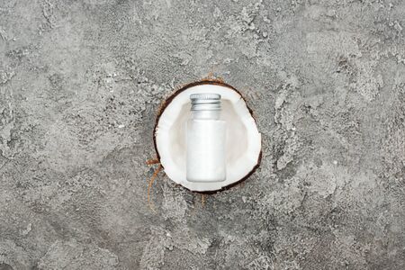 top view of cream in bottle on coconut half on grey textured backgroundの写真素材