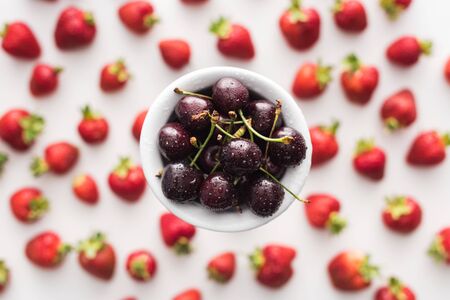 top view of sweet cherries on bowl and strawberries on background