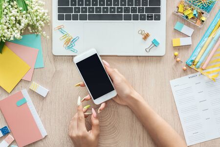 cropped view of woman sitting behind wooden table with laptop, weekly list, stationery and holding...