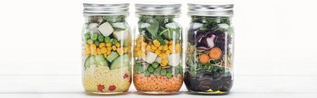 delicious vegetable salad in jars on wooden white table isolated on white, panoramic shot