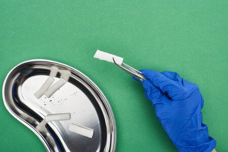 cropped view of dentist holding tweezers with cotton pad near metallic plate on green