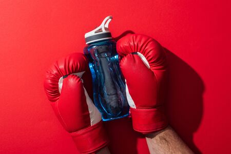 cropped view of boxer holding sport bottle with boxing gloves on redの写真素材