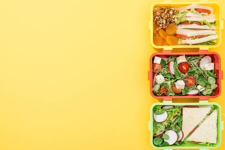 top view of three lunch boxes with food  on yellow background